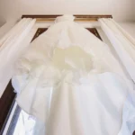 Abito da sposa bianco con gonna vaporosa appeso alla tenda della finestra | Fabio Zenoardo