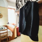 Giacca da cerimonia scura appesa su un attaccapanni in un interno rustico con fiori | Fabio Zenoardo
