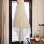 Abito da sposa appeso alla finestra con scarpe bianche e velo sul tavolo | Fabio Zenoardo