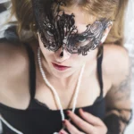 Primo piano dall'alto di modella con maschera di pizzo nera con diamanti, lingerie nera, collana di perle | Fabio Zenoardo