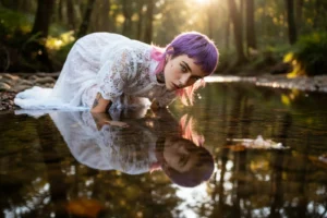 Modella con abito in pizzo sdraiata verso il proprio riflesso nell'acqua del ruscello