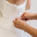 Mani allacciano il corsetto a nastri dell'abito da sposa bianco | Fabio Zenoardo fotografo