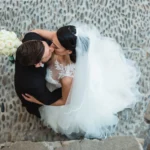 Sposi si baciano visti dall'alto in un caruggio di ciottoli ligure, abito bianco e bouquet | Fabio Zenoardo
