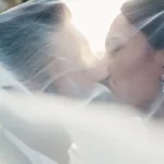 Bacio romantico degli sposi avvolti nel velo bianco, retroilluminati dal tramonto | Fabio Zenoardo