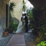 Sposi si baciano in un cortile con arco e piante mediterranee, velo lungo | Fabio Zenoardo