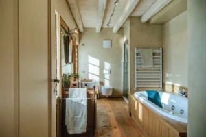 Bagno in casale di lusso con vasca grande, box doccia, lavabo in legno e travi a vista, pavimento in parquet