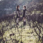 Due ragazze in abito nero si guardano tra la vegetazione secca, controluce, fotografia moda Imperia