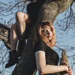 Vista dal basso, una modella in cima all'albero e una sotto con orsacchiotto, controluce, moda Fabio Zenoardo