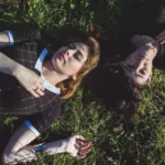 Due modelle sdraiate nell'erba riprese dall'alto, abiti neri, fotografia moda Liguria