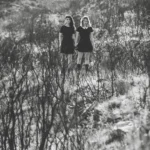 Fotografia in bianco e nero di due ragazze in abito nero tra la vegetazione bruciata, moda Fabio Zenoardo fotografo Liguria
