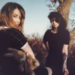 Modella con orsacchiotto guarda l'altra di fianco, controluce tra gli alberi, fotografia moda Fabio Zenoardo