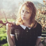 Ritratto di modella bionda tra rami spogli in controluce, espressione intensa, fotografia moda Imperia