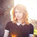 Ritratto di modella bionda con luce solare dorata, vicino a tronco, atmosfera luminosa, fotografia moda
