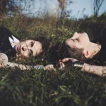 Due ragazze sdraiate nell'erba fianco a fianco, occhi chiusi, atmosfera intima, fotografia fashion