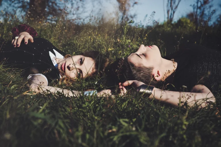 Due ragazze sdraiate nell'erba fianco a fianco, occhi chiusi, atmosfera intima, fotografia fashion