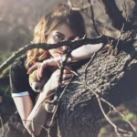 Modella che sbircia tra i rami spogli, orecchino pendente, sguardo curioso, fotografia moda Liguria