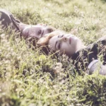 Due ragazze sdraiate tra fiori selvatici, luce soffusa, atmosfera onirica, fashion photography Fabio Zenoardo