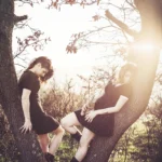 Due modelle tra alberi con luce calda di tramonto, una tiene l'orsacchiotto, fotografia fashion Imperia