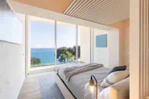 Camera da letto moderna con tre finestre panoramiche, vista sul mare e palme, pavimento in parquet chiaro