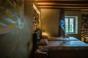 Camera da letto rustica con pareti in pietra, travi in legno a vista, illuminazione calda e vassoio colazione sul letto