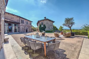 Casale di lusso in pietra con ampia terrazza esterna, tavolo da pranzo outdoor, ulivo e vista mare in lontananza