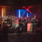 Band al completo sul palco con luci rosse e blu, atmosfera rock, evento Imperia