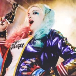 Cosplay Harley Quinn con pistola dorata e giacca viola metallizzata, makeup colorato, fotografia cosplay Fabio Zenoardo