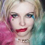 Primo piano del makeup Harley Quinn con ombre fucsia e azzurro, labbra rosse, neo finto, choker Daddy