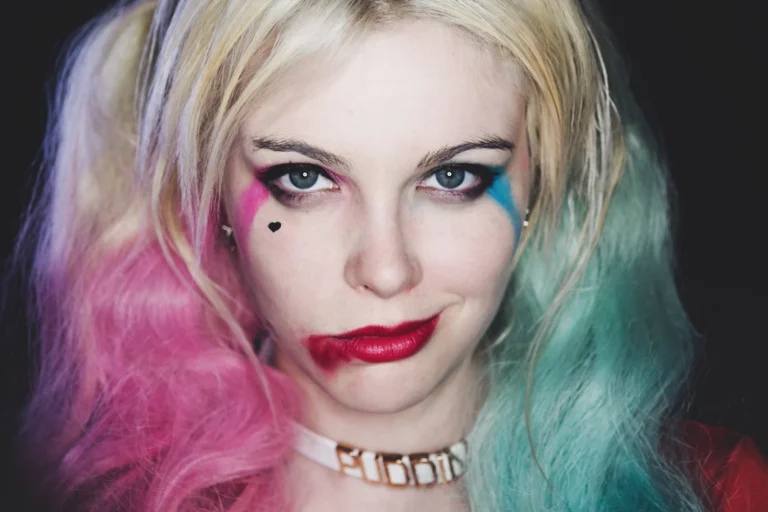 Primo piano del makeup Harley Quinn con ombre fucsia e azzurro, labbra rosse, neo finto, choker Daddy