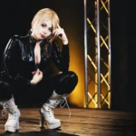 Yuriko Tiger accovacciata sul palco con stivali platform bianchi, tuta latex, luce drammatica, cosplay photography