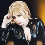 Primo piano di Yuriko Tiger in latex nero, capelli biondi, sguardo intenso, fotografia cosplay moda Imperia