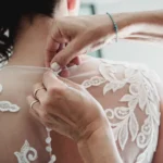 Dettaglio dell'abito da sposa in pizzo con piccoli bottoni mentre viene allacciato | Fabio Zenoardo