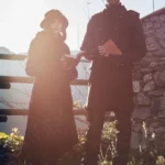 Coppia in costume dark con libri, posa scenica controluce solare, ambientazione medievale