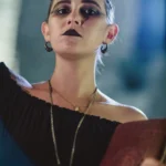 Primo piano attrice Ghost Tour con makeup dark, labbra nere, libro rosso, luce teatrale blu
