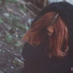 Fotografo artistico Liguria - modella cappuccio testa bassa bosco scuro