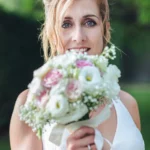 Sposa bionda con occhi azzurri tiene il bouquet vicino al viso in giardino | Fabio Zenoardo