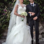 Sposi posano sorridendo davanti a un muro con bouganvillea e rose, lo sposo con bastone | Fabio Zenoardo