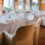 Sala ricevimento allestita con sedie bianche foderate e tavoli con tovaglie bianche, finestre panoramiche | Fabio Zenoardo