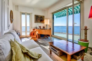 Salotto con divano, tavolino in legno, arredamento eclettico e ampia vista frontale sul mare dalla terrazza