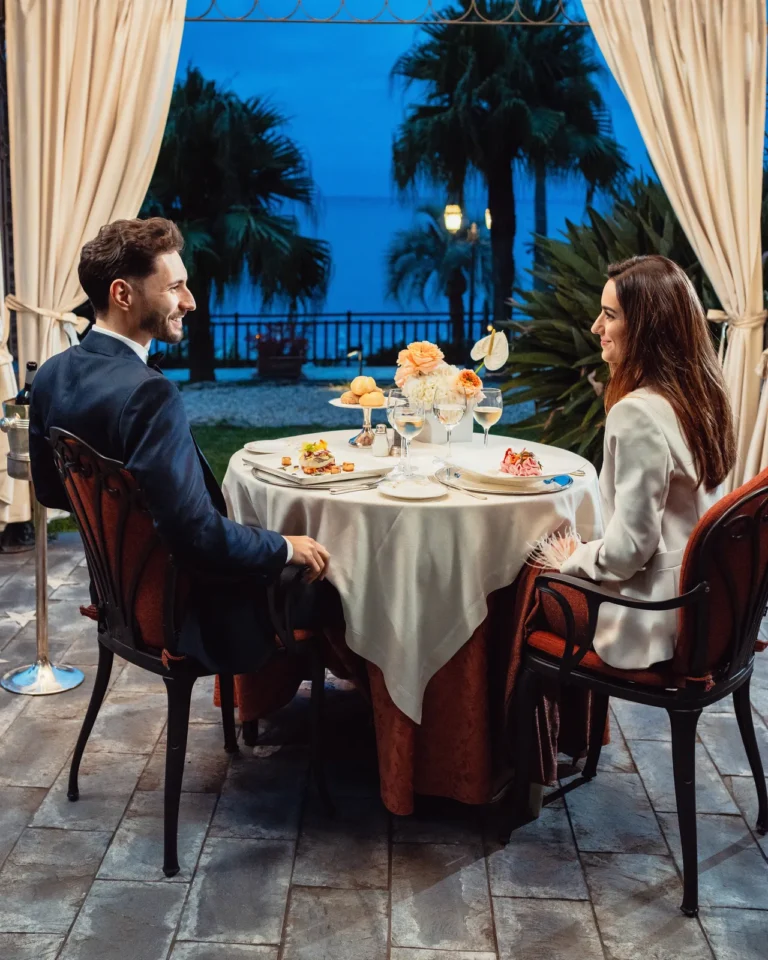 Coppia a cena in terrazza elegante di notte, ristorante con palme e vista sul mare, Royal Hotel Sanremo