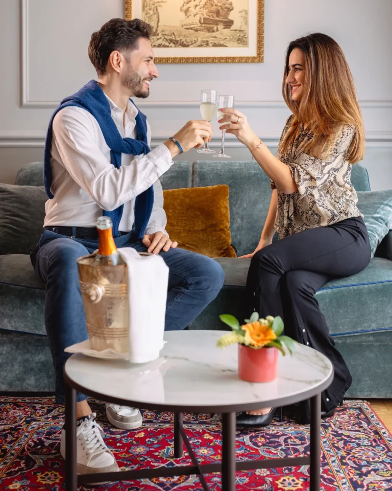 Coppia sorridente che brinda con flute di champagne in salotto lussuoso con divano blu, Royal Hotel Sanremo