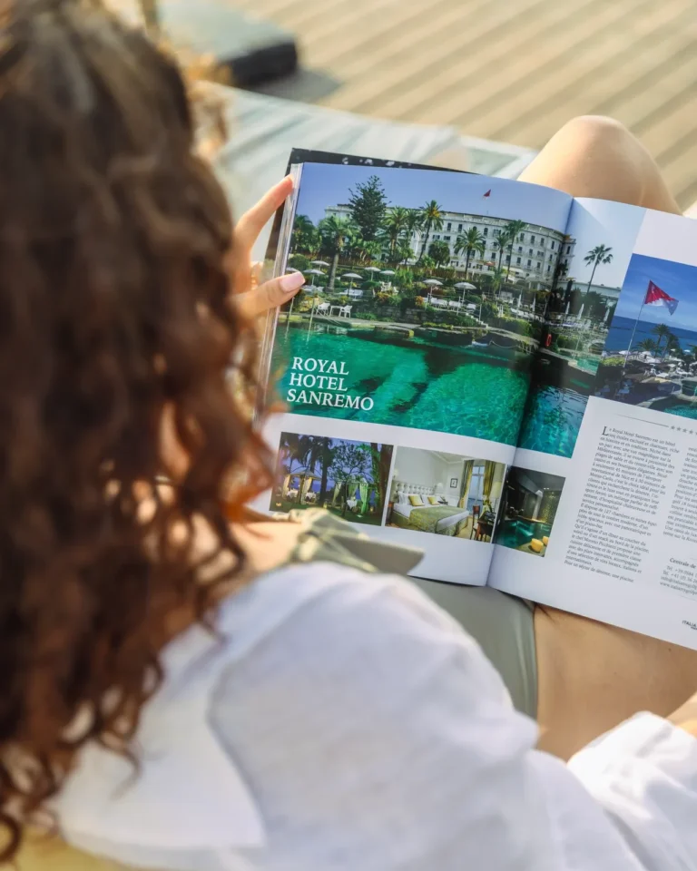 Donna di spalle che legge rivista con Royal Hotel Sanremo in copertina, bordo piscina