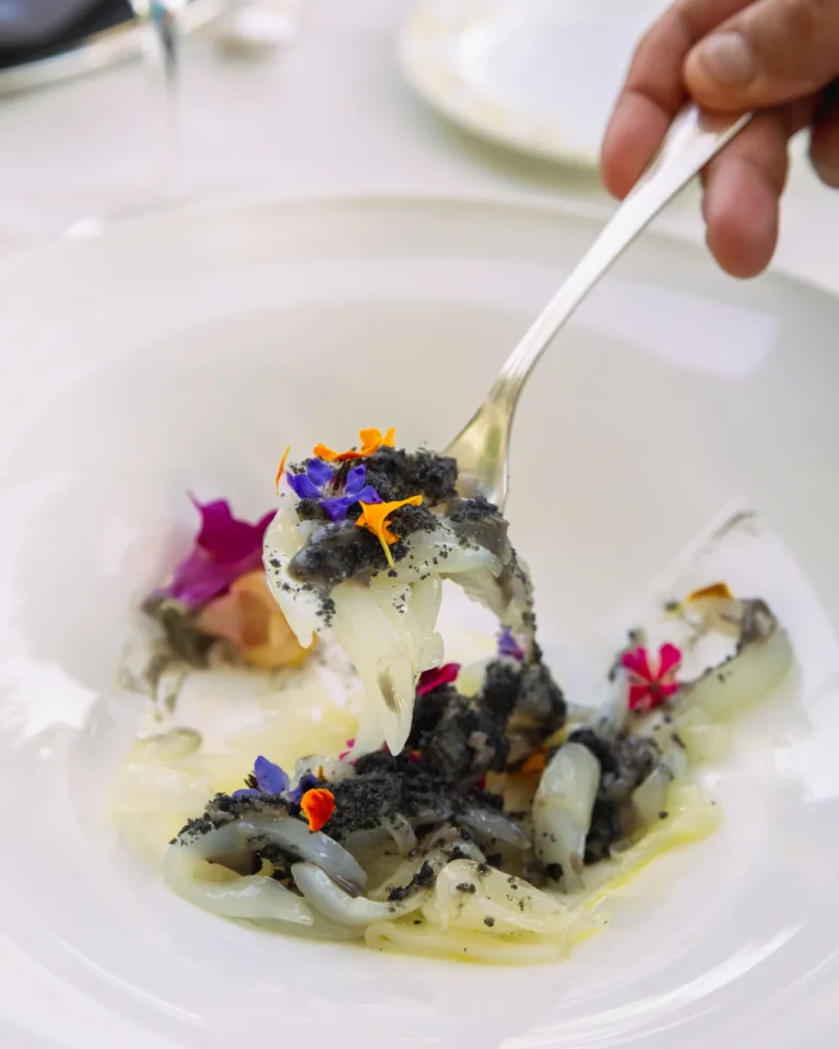 Piatto gourmet con pasta e fiori eduli colorati su forchetta, food photography fine dining