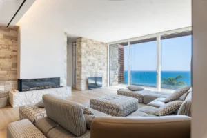 Soggiorno di lusso con camino in pietra, divano modulare e parete vetrata con vista sul mare, Liguria