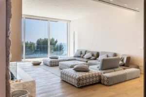 Ampio soggiorno con divano modulare, grande finestra con vista mare e vegetazione, villa di lusso Liguria