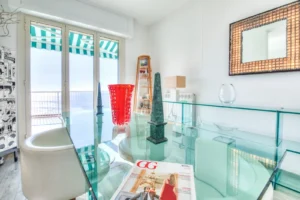 Soggiorno di appartamento di lusso con tavolo in vetro, oggetti di design, rivista GG e vista mare con tenda a righe