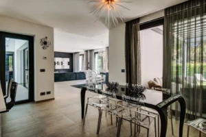 Sala da pranzo con tavolo in vetro nero e sedie crystal, lampadario sputnik, soggiorno open space con pareti scure