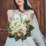 Sposa con tatuaggi sulle spalle tiene bouquet di rose bianche con edera e velo | Fabio Zenoardo