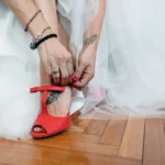 Sposa in abito bianco allaccia la scarpa rossa con tacco, tatuaggio visibile sul piede | Fabio Zenoardo