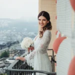 Sposa sorride sul balcone con rose bianche, paesaggio cittadino lacustre sullo sfondo | Fabio Zenoardo